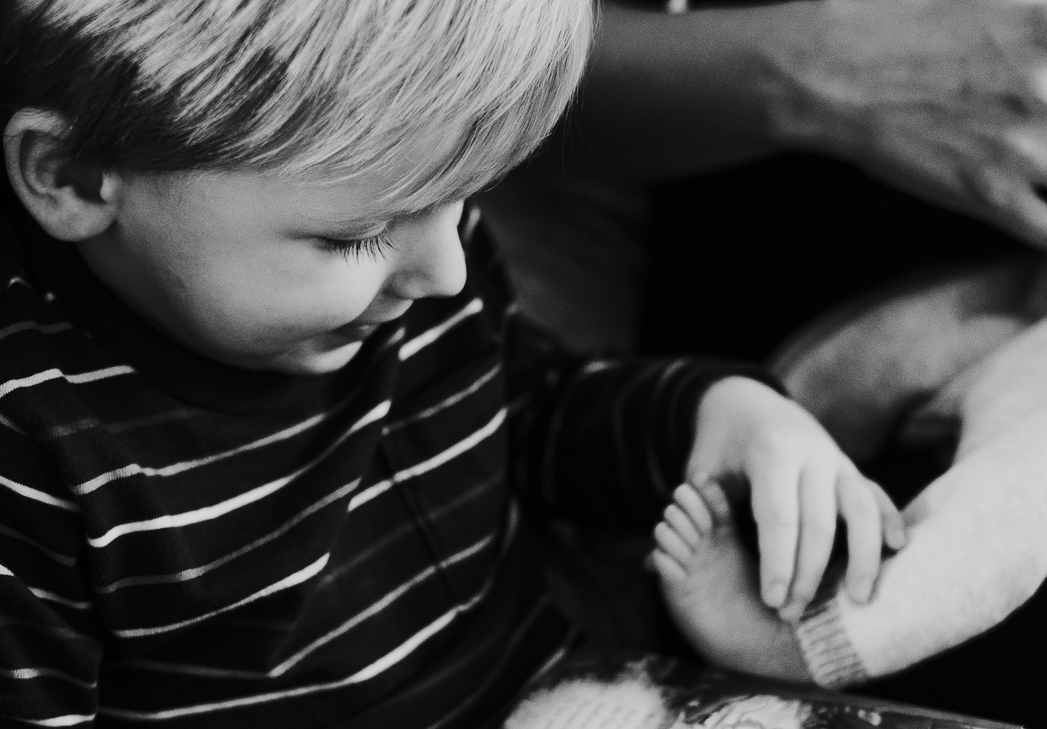 toddler boy holding baby brothers foot black and white photo london newborn photography