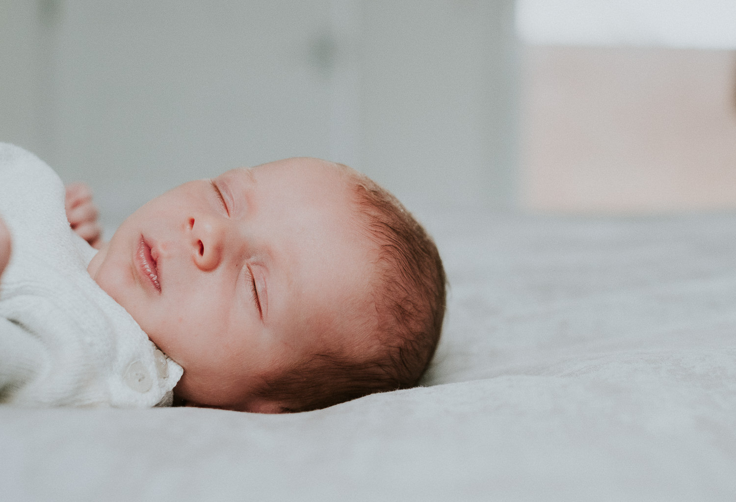 baby with eyes closed lying on bed natural light