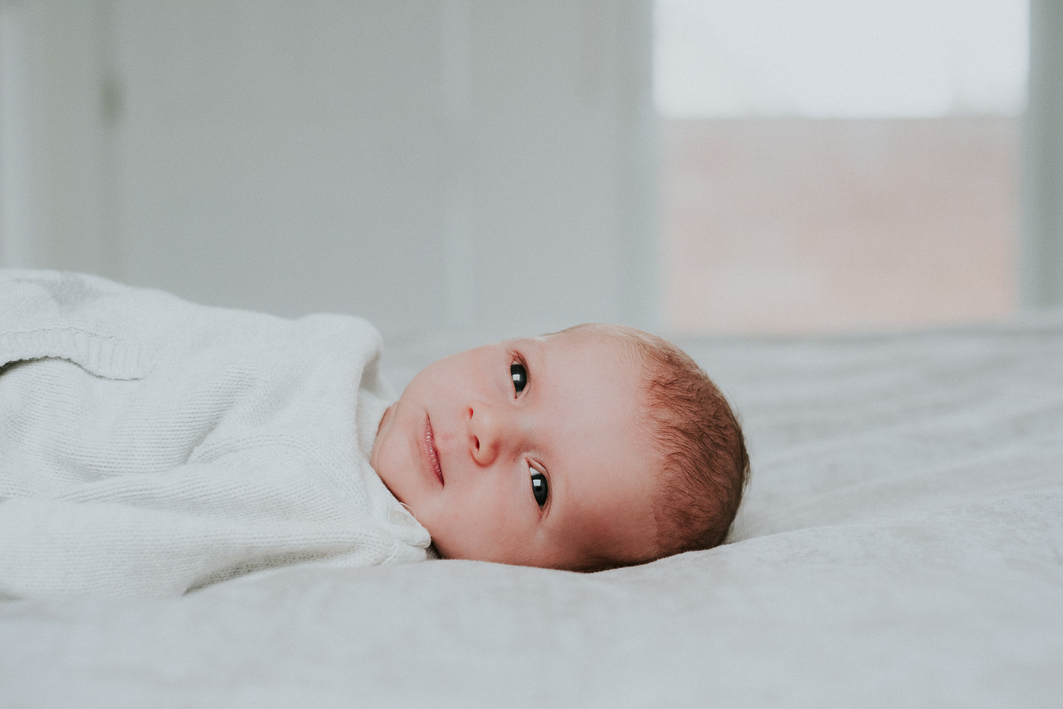 newborn baby boy with eyes open lying on bed natural light