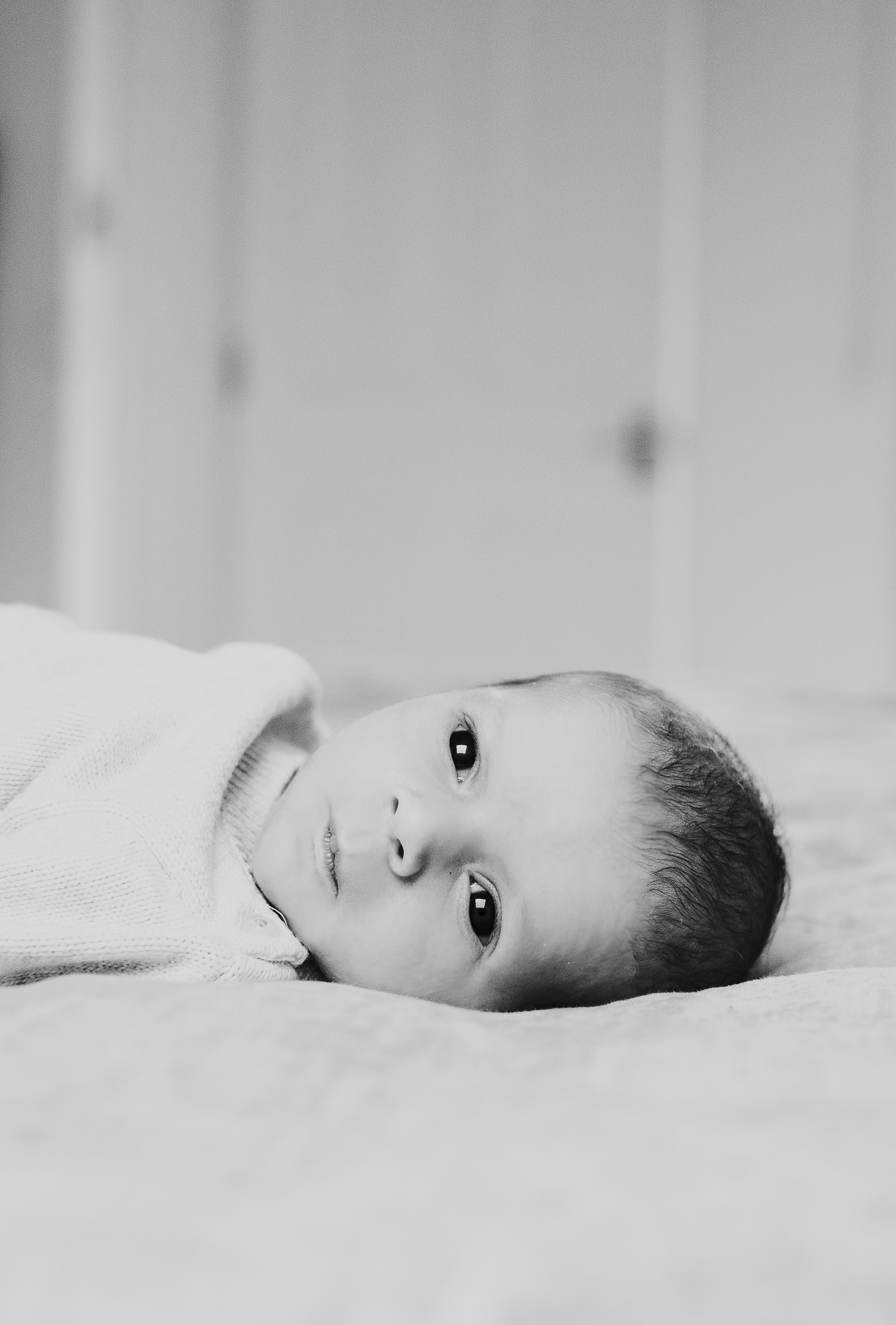 newborn baby boy with eyes open lying on bed natural light