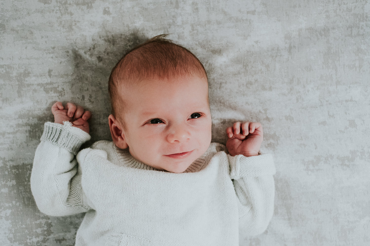 newborn baby boy with eyes open lying on bed natural light