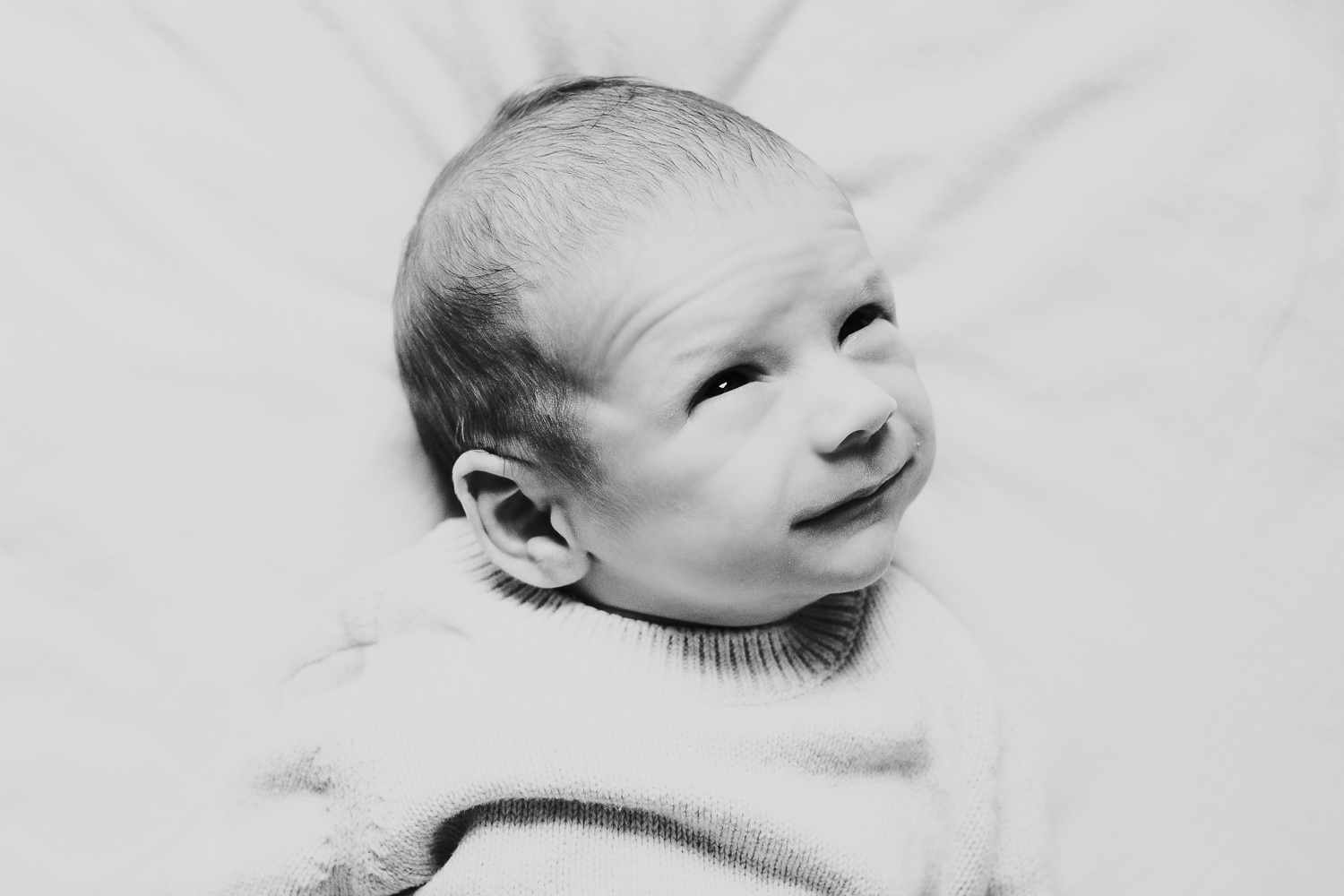 newborn baby boy with eyes open lying on bed natural light