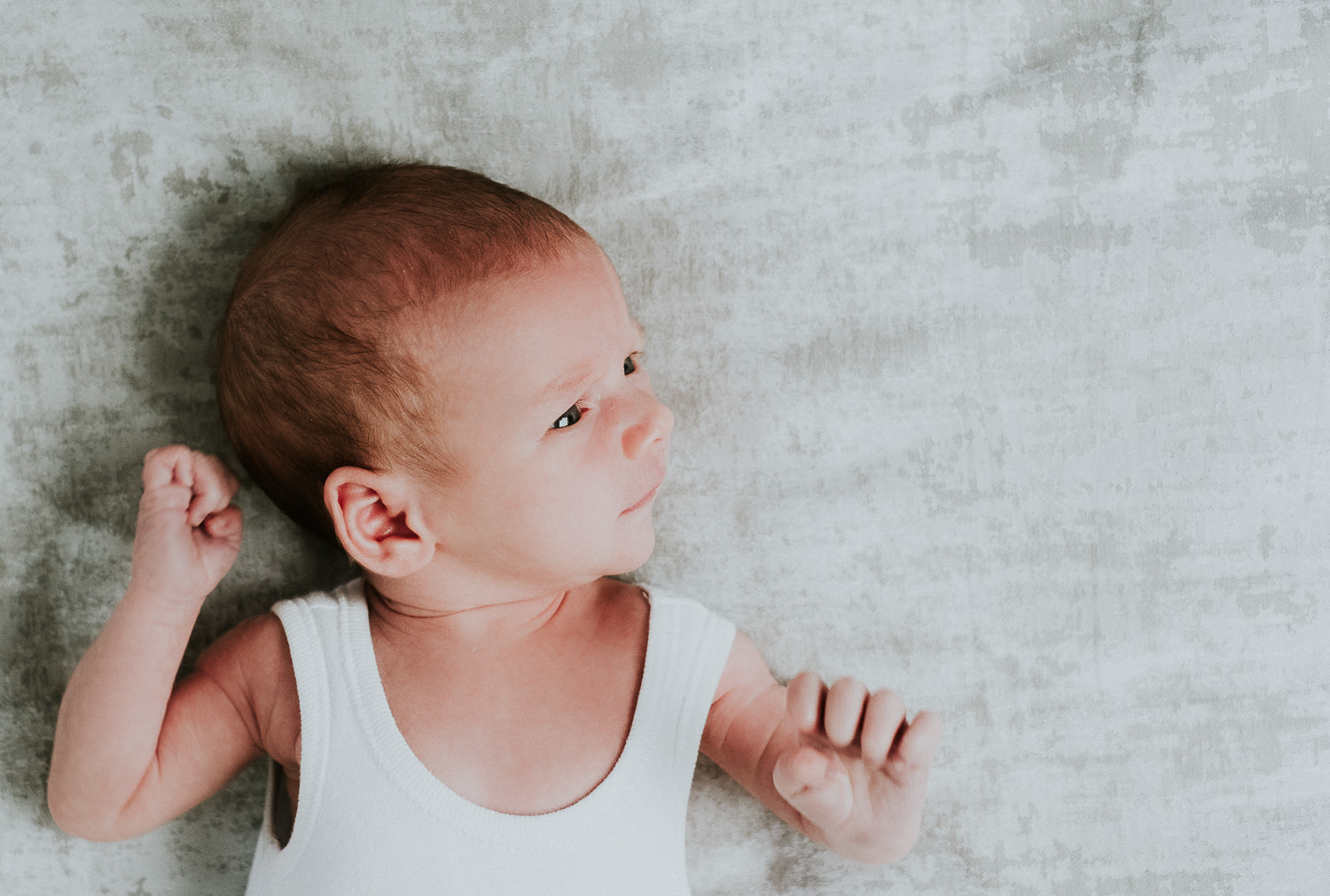 newborn baby boy with eyes open lying on bed natural light