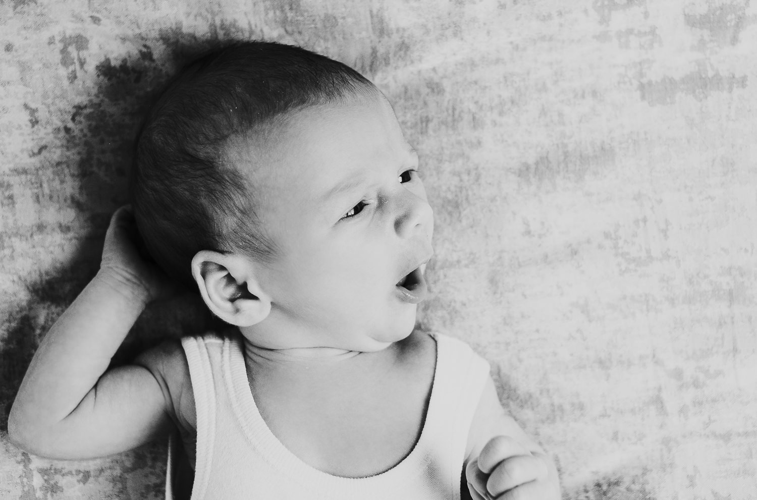 newborn baby boy with eyes open lying on bed natural light