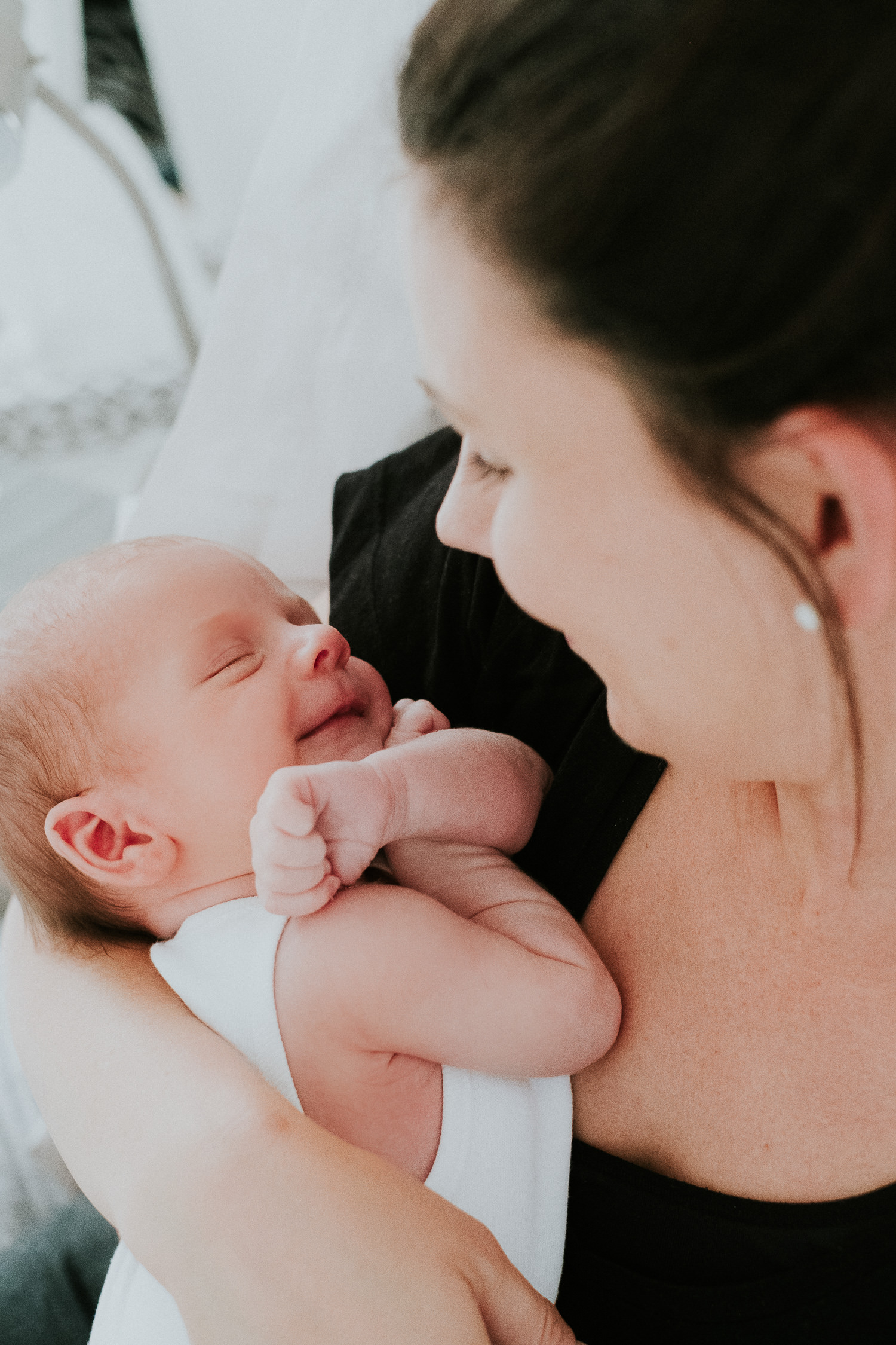 newborn baby boy smiling lying in mother's arms natural light