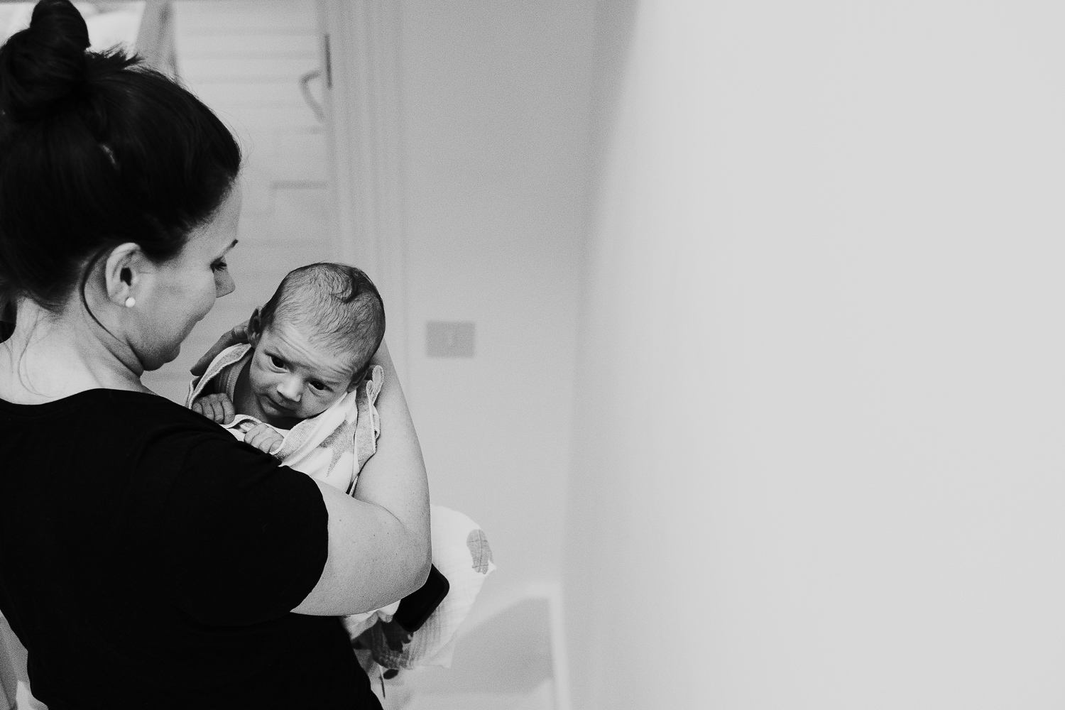 newborn baby boy being carried downstairs in mothers arms black and white photo