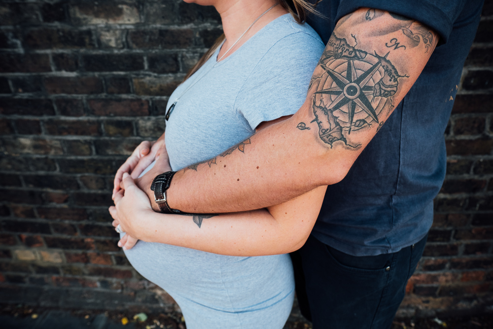 CLOSE UP OF PREGNANCY BUMP AND TATTOOED ARMS AROUND
