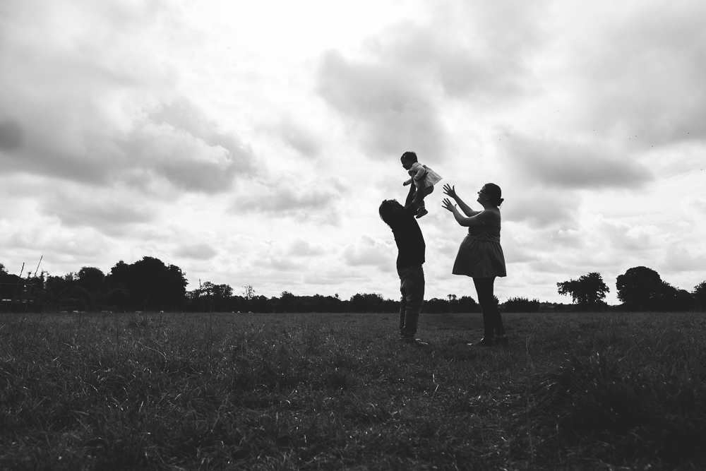 PREGNANT WOMAN AND PARTNER THROWING CHILD IN AIR IN FIELD