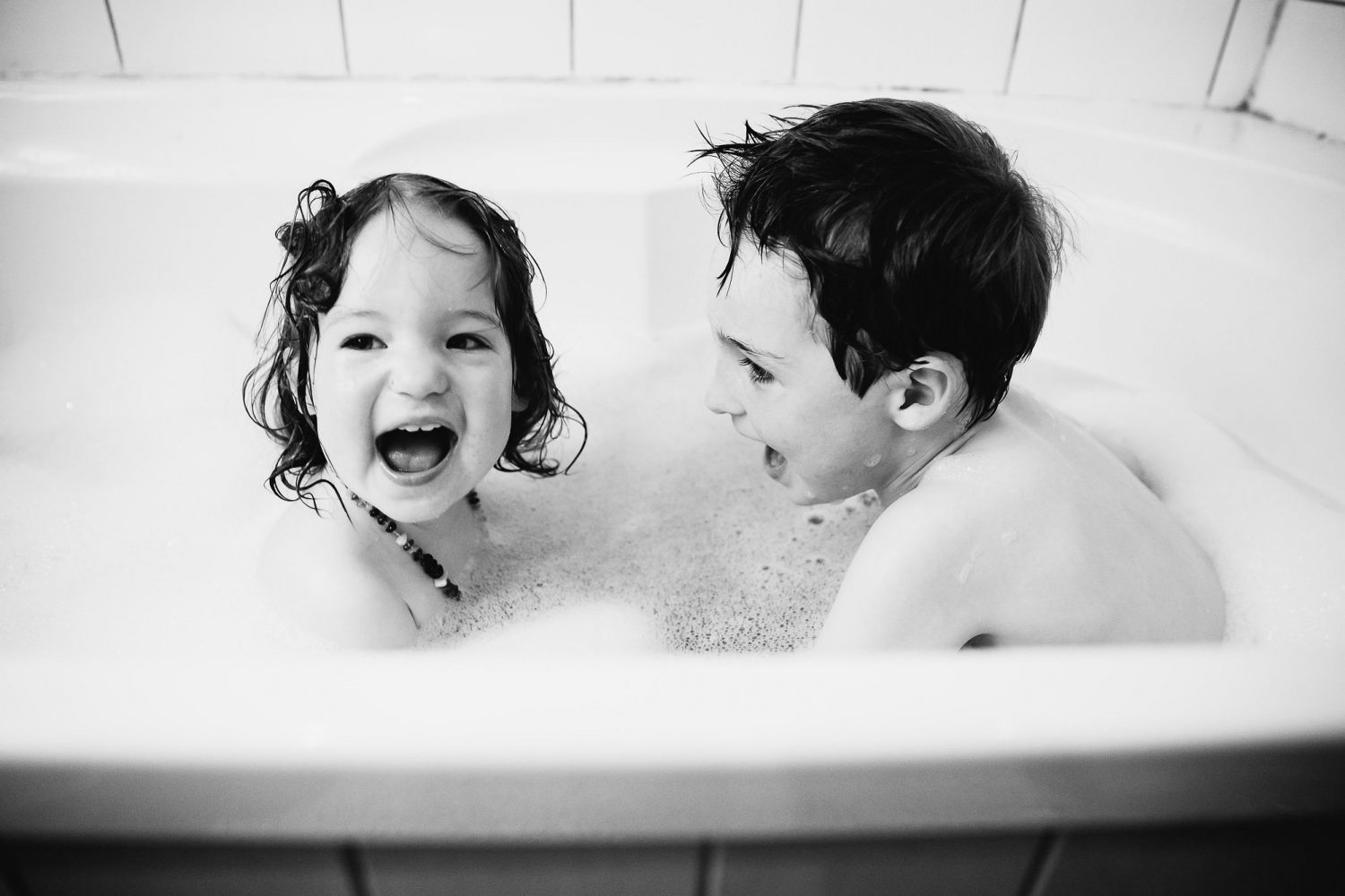 young siblings brother and sister having fun in the bath with lots of bubbles