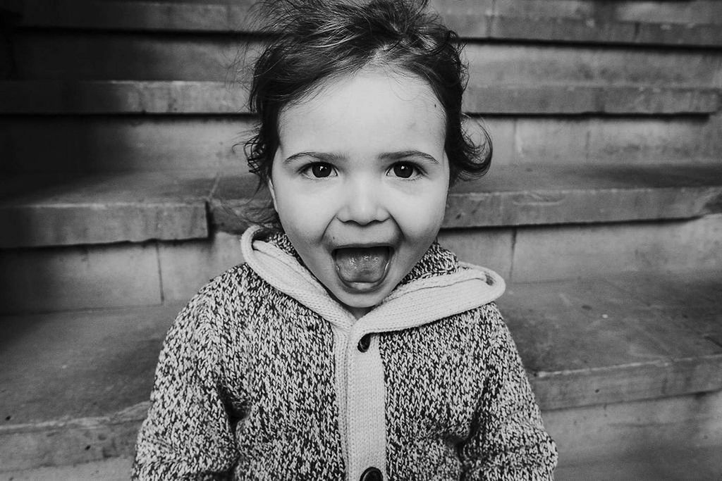 black and white photo of toddler girl sticking tongue out