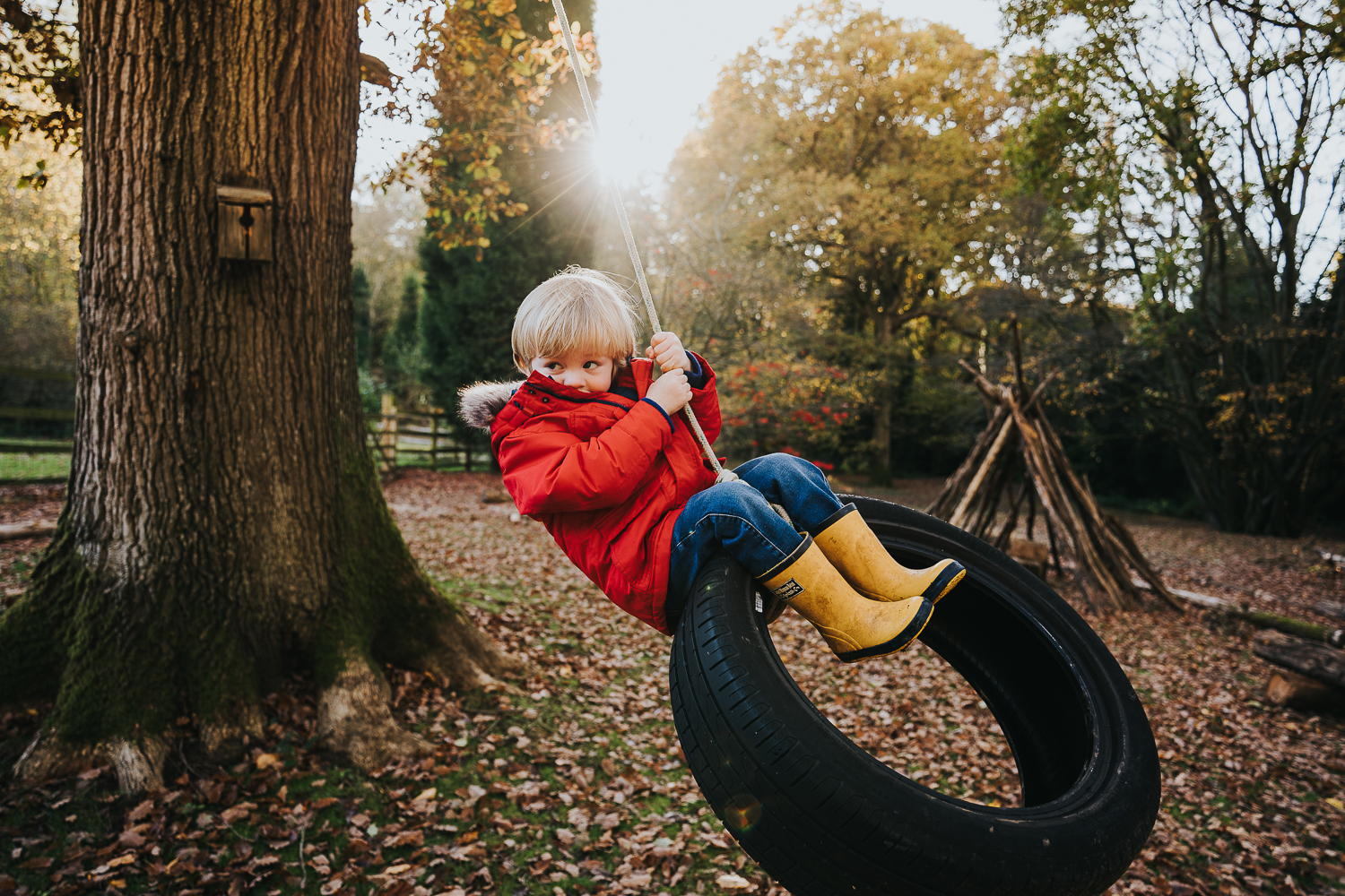 London family photography 2020 young boy swinging on tyre swing in autumn sunshine
