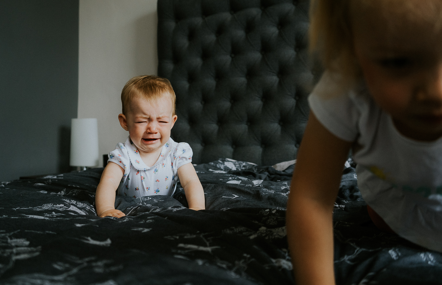 family photography 2020 baby crying on bed whilst siblings crawls away