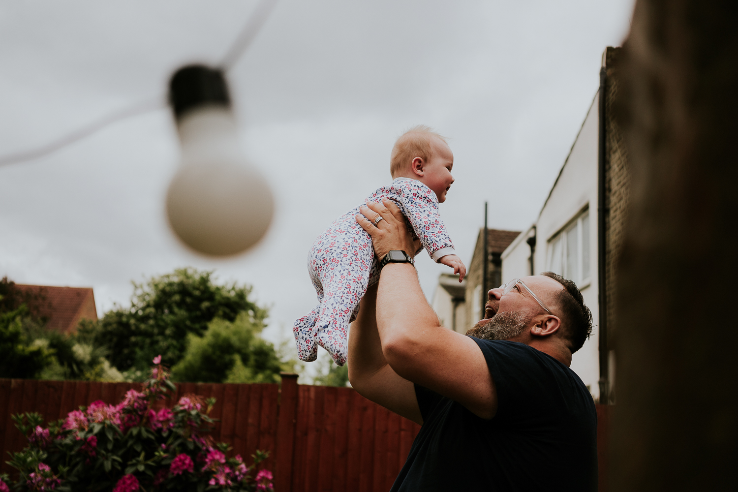 day in the life photo shoot father holding baby daughter in the air grey clouds behind