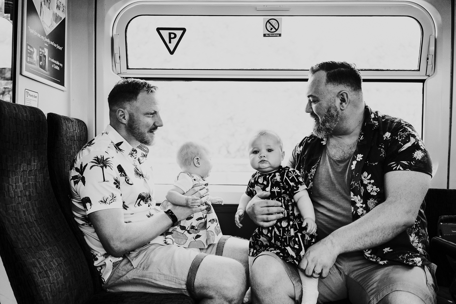 day in the life photo shoot two fathers and twin baby girls on train black and white shot