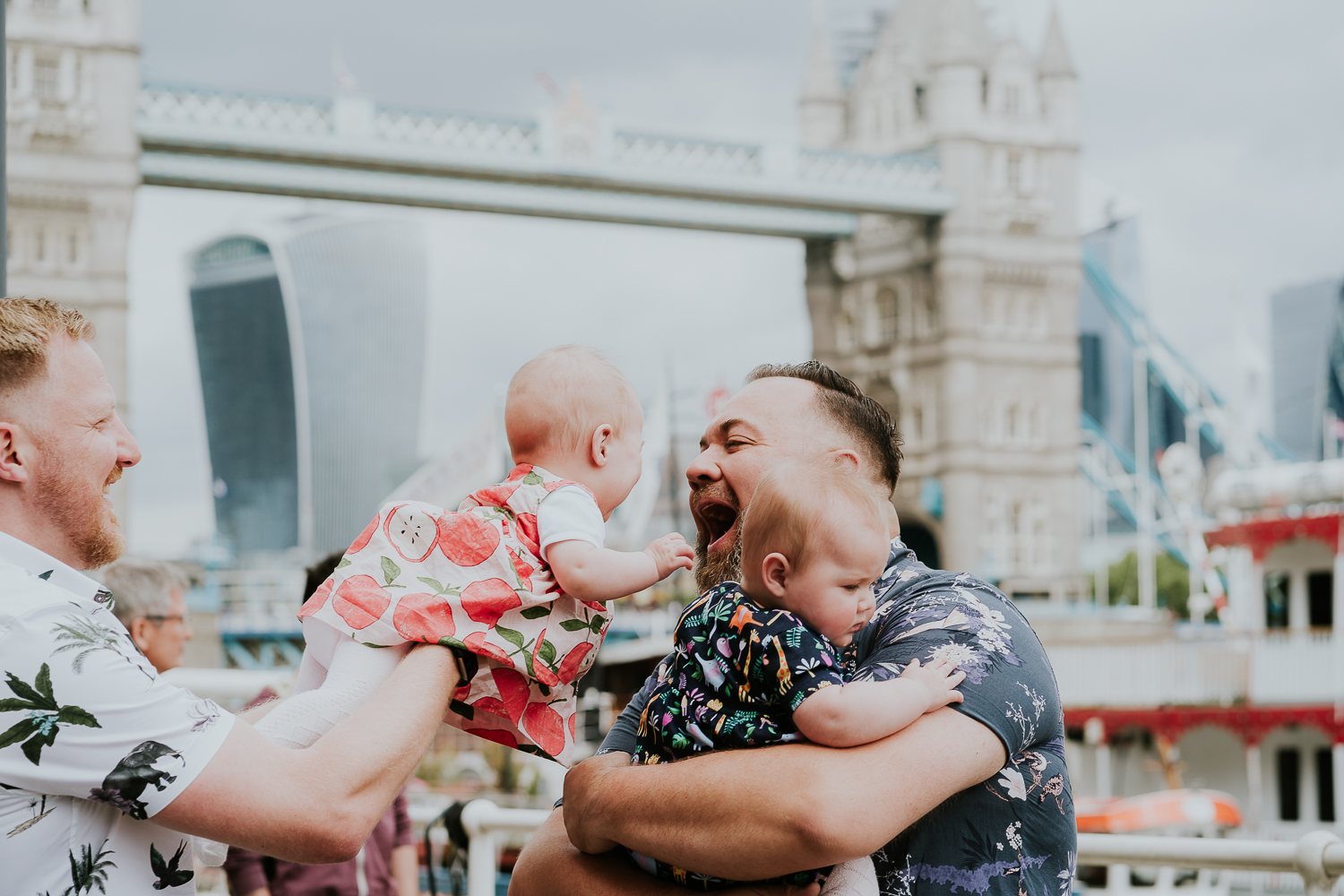 day in the life photo shoot two dads with twin baby girls playing with view of Tower Bridge in background