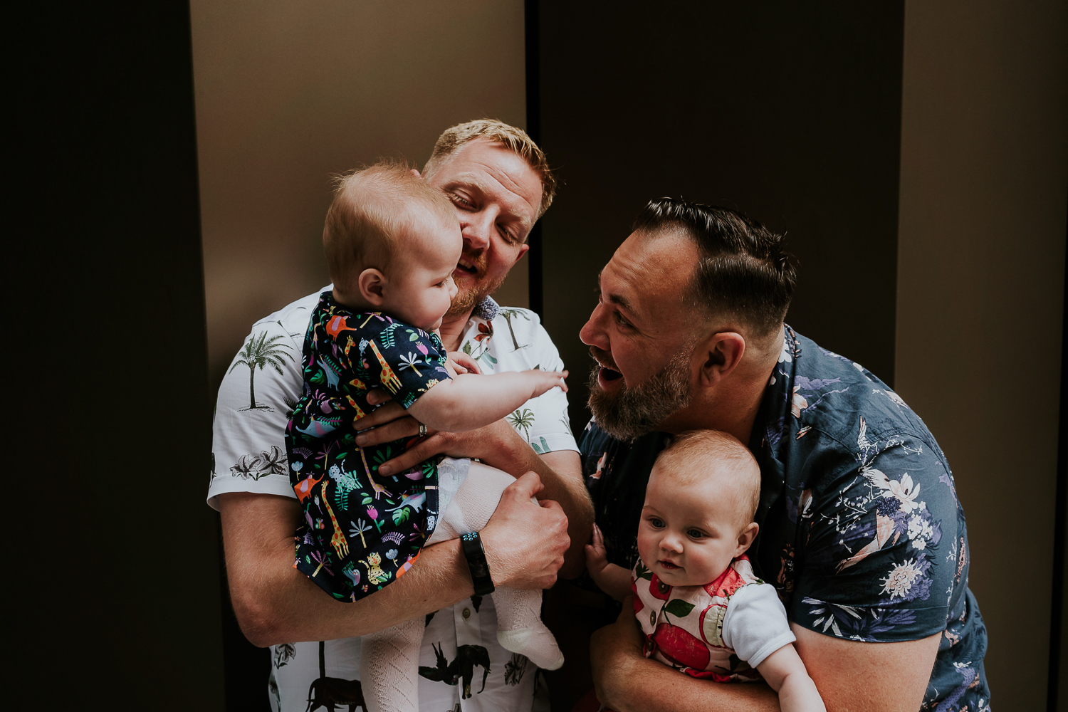 day in the life photo shoot two dads with twin baby girls playing against dark wall