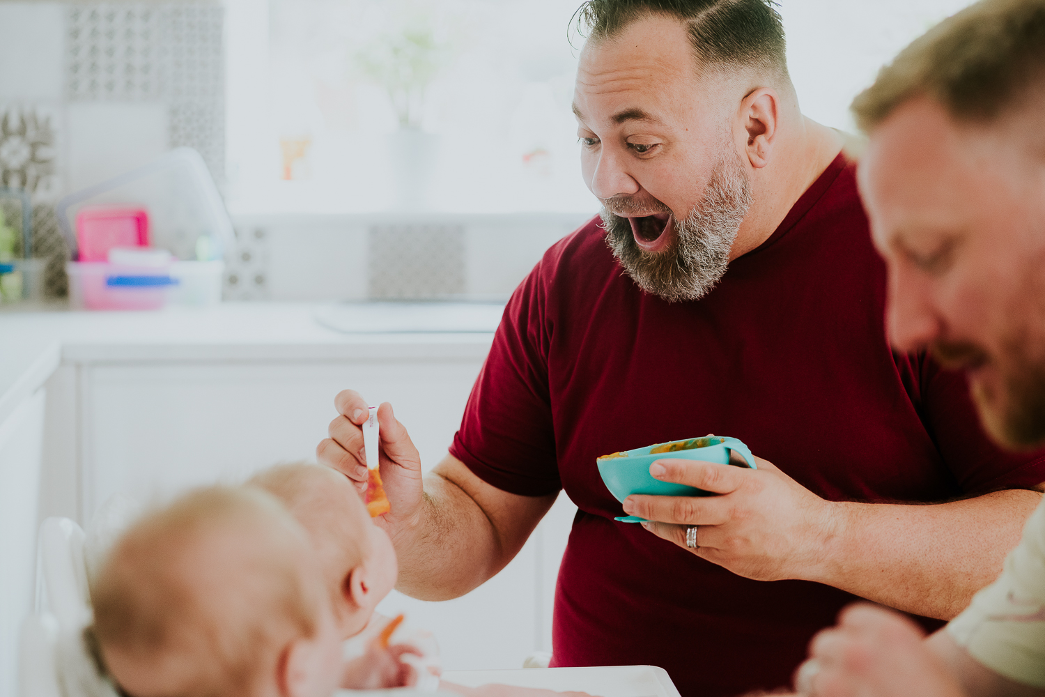 day in the life photo shoot father smiling expression as he spoon feeds baby girl