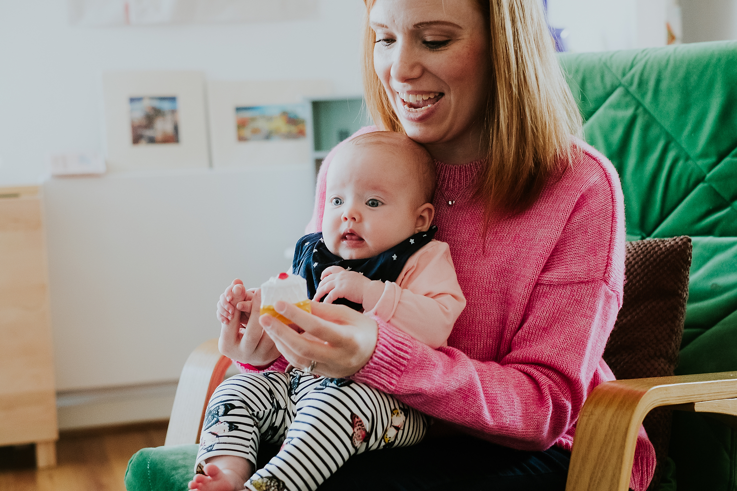 home scene of mother with baby on lap holding pretend piece of cake playing with make believe toys islington family photographer shoot