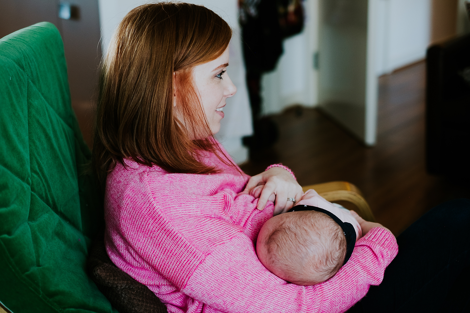 mother in pink jumper breastfeeding baby on green chair at home islington family photographer