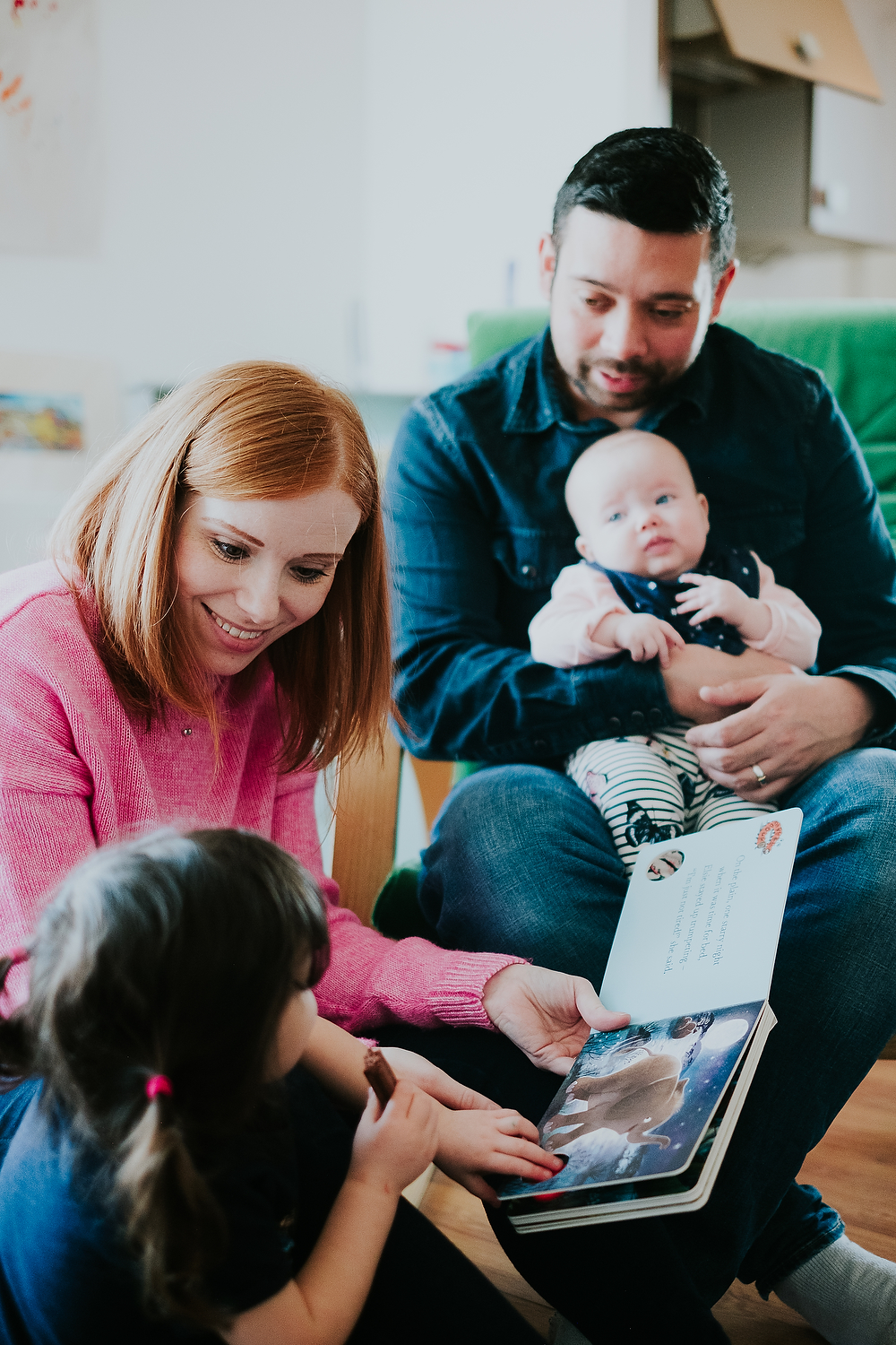 mother reading book to toddler daughter whilst father and baby daughter look on at home islington family photographer