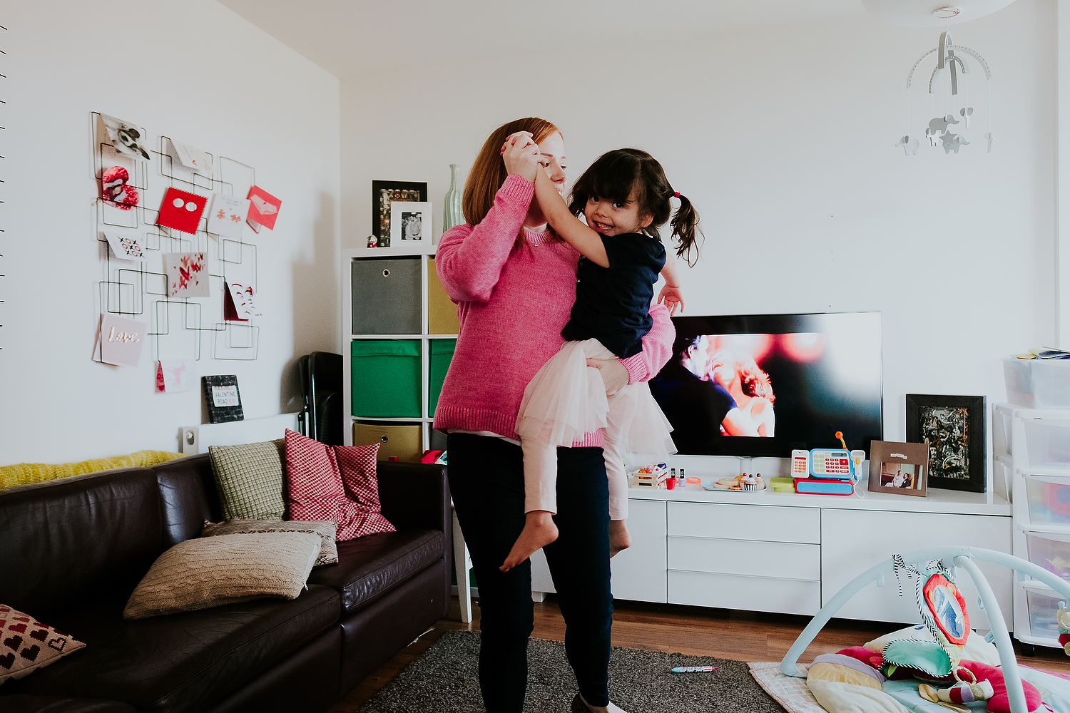 islington family photographer mother and toddler daughter dancing in living room at home with dirty dancing movie on tv in background