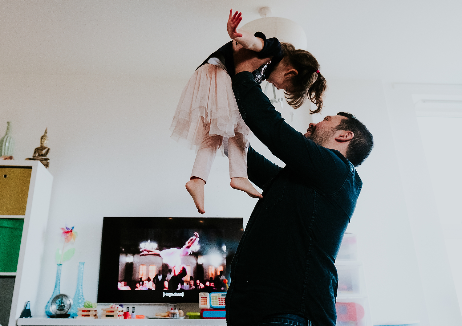 islington family photographer dad and toddler daughter dancing in living room at home with dirty dancing movie on tv in background