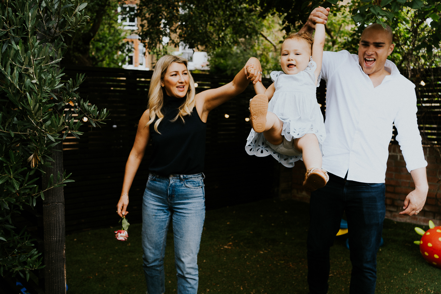 parents swinging toddler daughter and laughing NORTH KENSINGTON FAMILY PHOTO SESSION