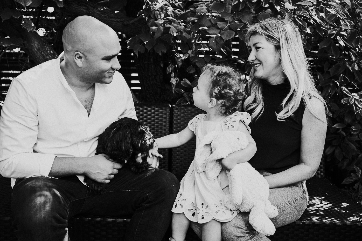 NORTH KENSINGTON FAMILY PHOTO SESSION black and white shot of family and dog sitting on sofa in garden