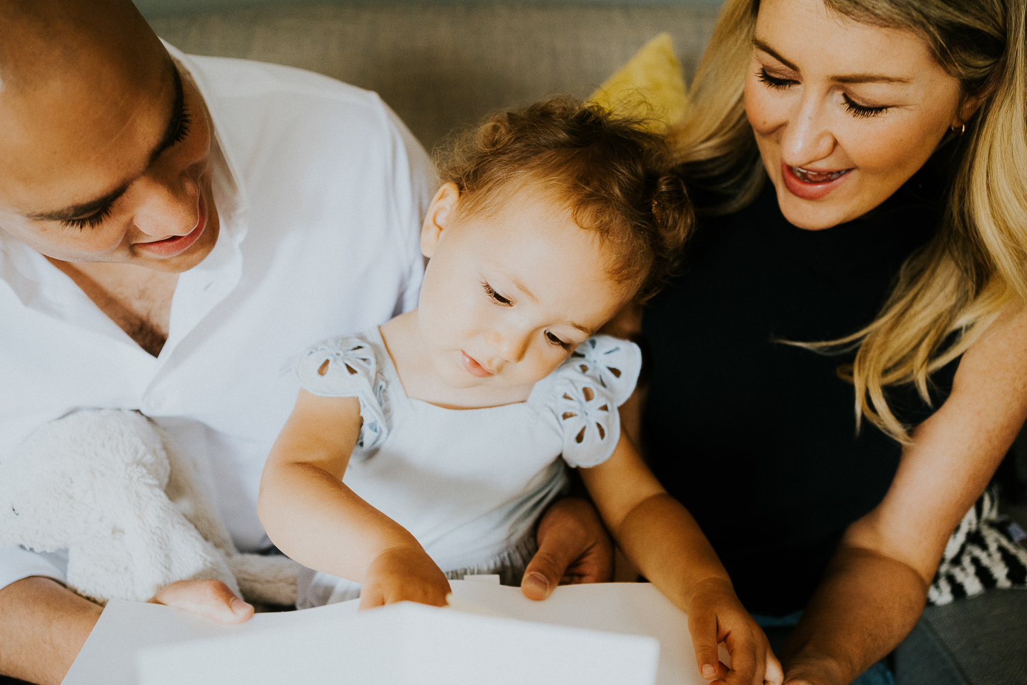 north kensington family photo session parents reading book with daughter toddler on sofa