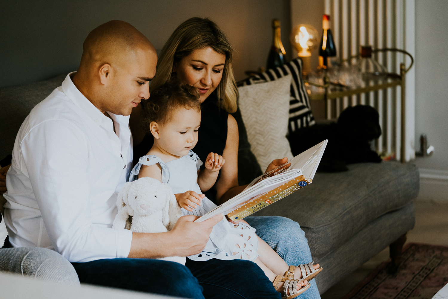 north kensington family photo session parents reading book with daughter toddler on sofa