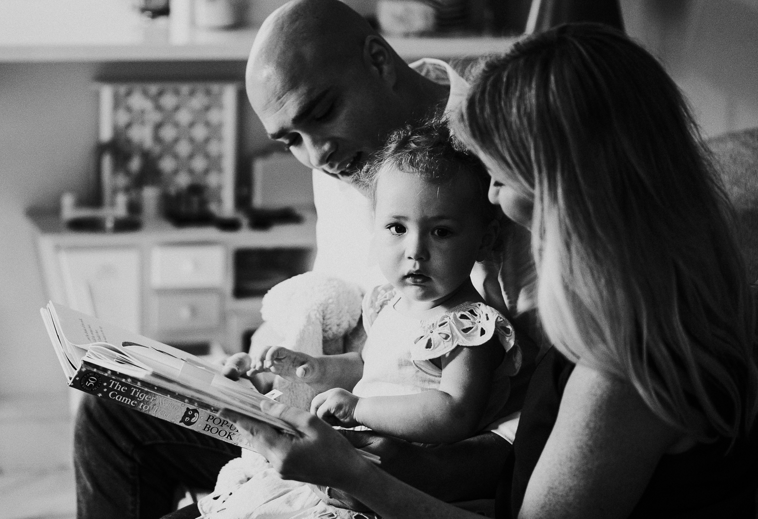 north kensington family photo session parents reading book with daughter toddler on sofa