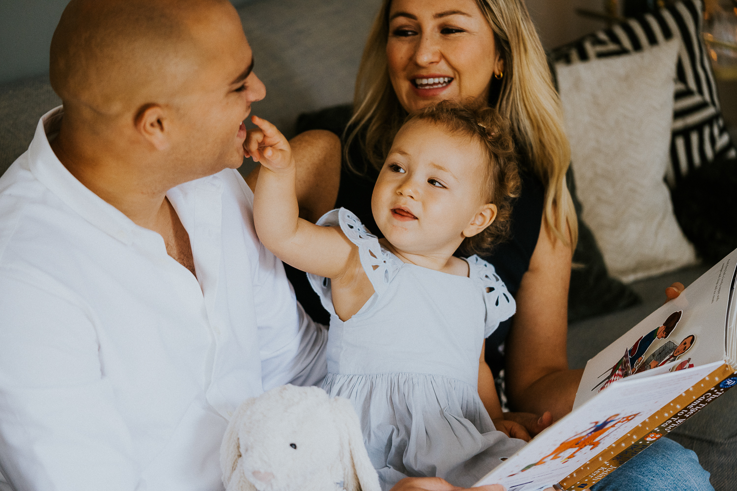 north kensington family photo session parents reading book with daughter toddler on sofa