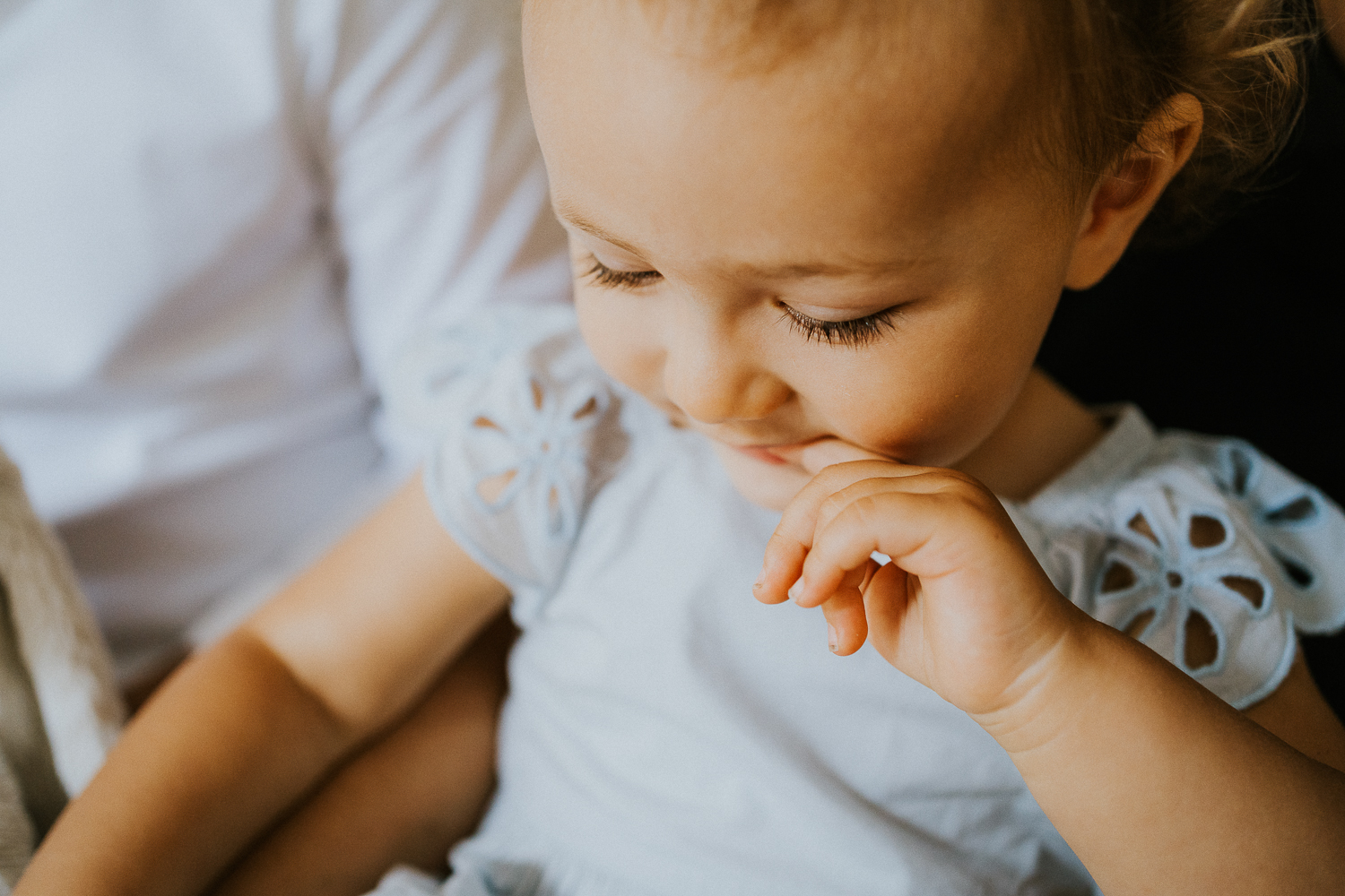 NORTH KENSINGTON FAMILY PHOTO SESSION toddler girl close up of eyelashes looking down at book with finger in mouth