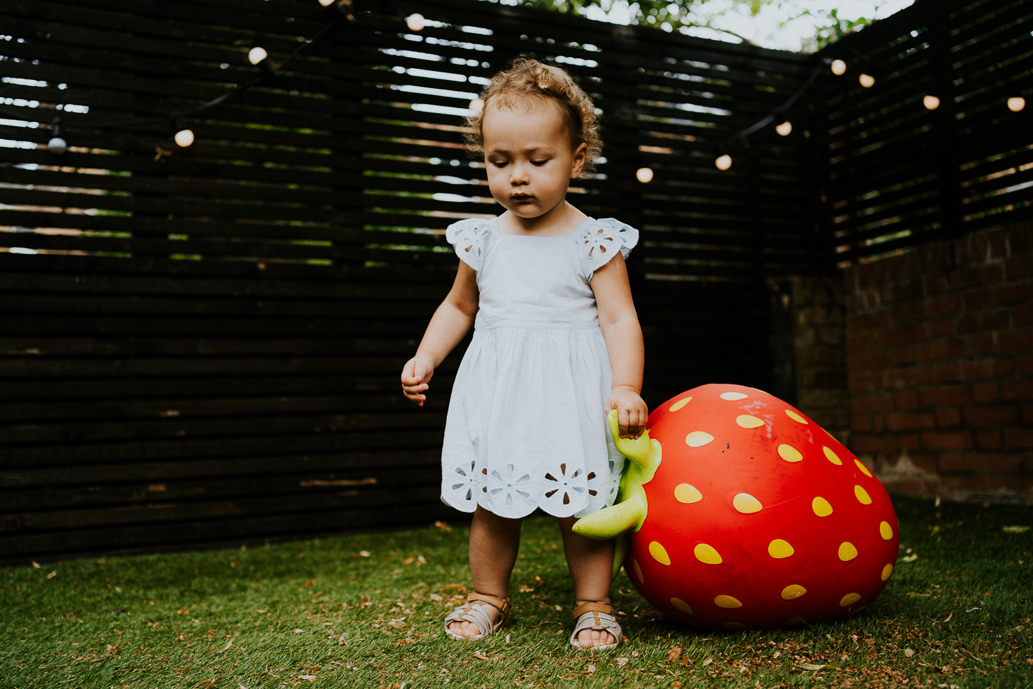 toddler girl playing with giant strawberry toy in garden NORTH KENSINGTON FAMILY PHOTO SESSION