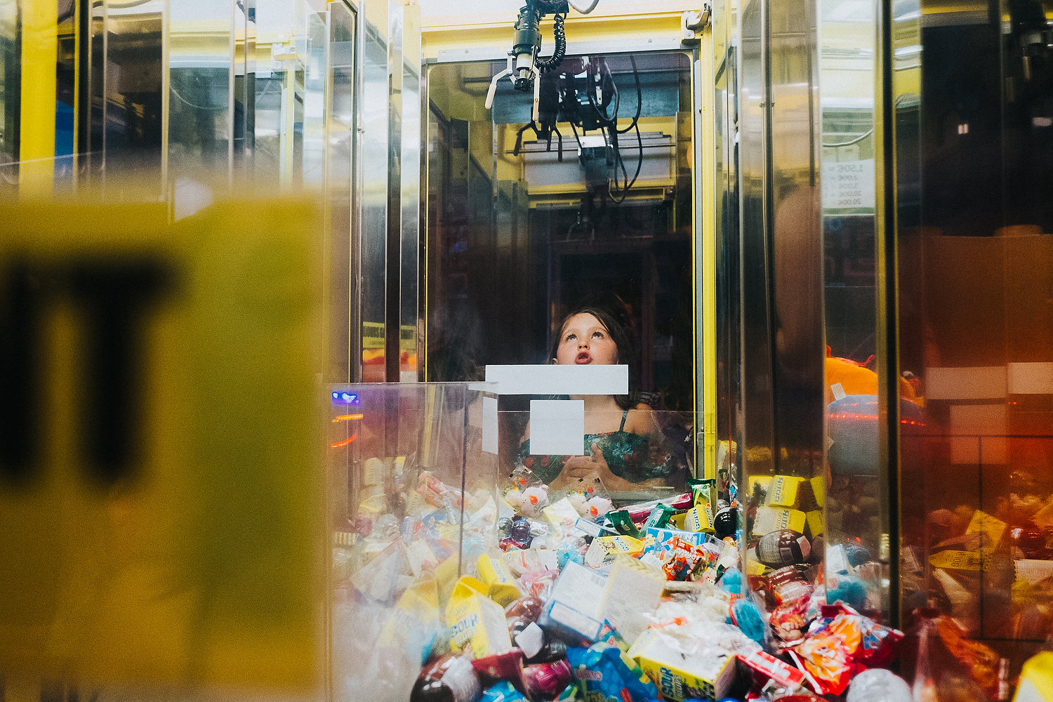 REAL LIFE FAMILY PHOTOS LITTLE GIRL PLAYING ON GRAB TOY MACHINE AND LOOKING UP AT CLAW HOPEFULLY TO WIN A PRIZE
