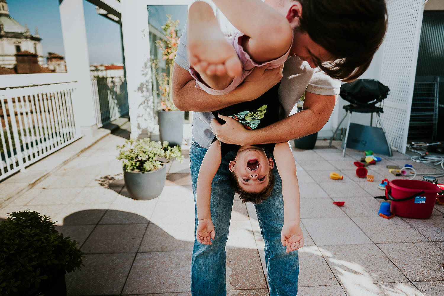 REAL LIFE FAMILY PHOTOS LITTLE BOY ON PATIO BEING HELD UPSIDE DOWN BY DAD AND LAUGHING
