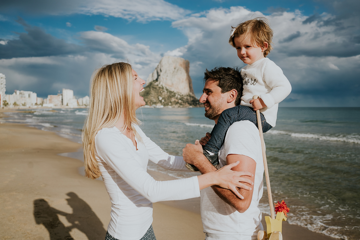 BOOKING A FAMILY PHOTO SESSION MOTHER, FATHER AND DAUGHTER LAUGHING ON BEACH
