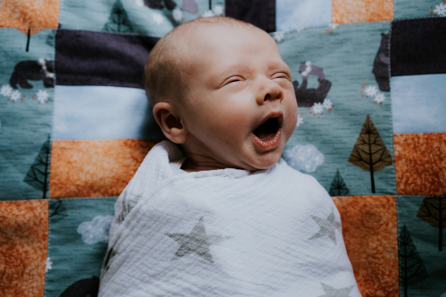 newborn photo session at home in highgate photo of baby boy yawning swaddled on patchwork quilt