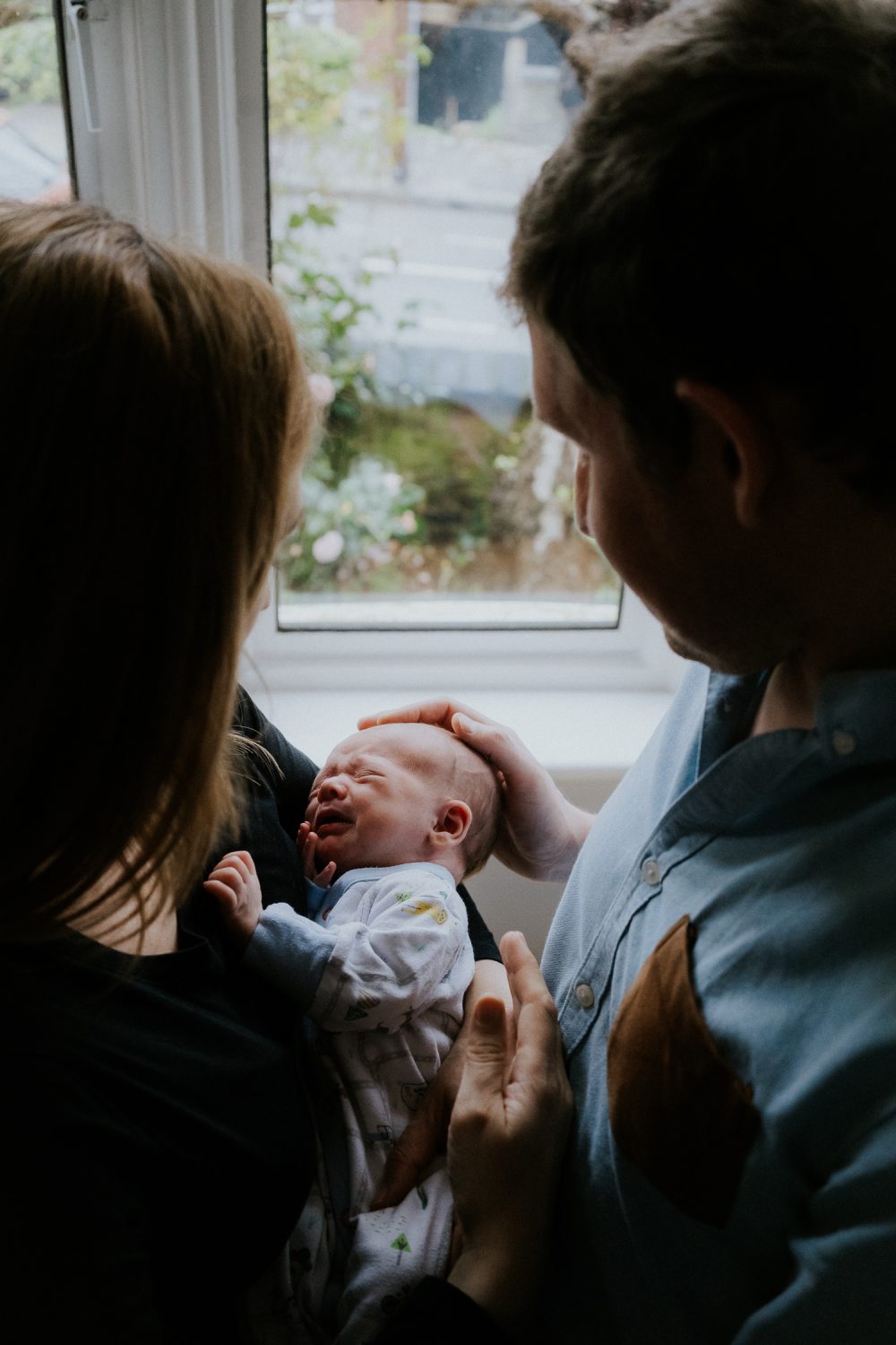 newborn photo session at home in highgate photo of baby boy crying with parents holding him