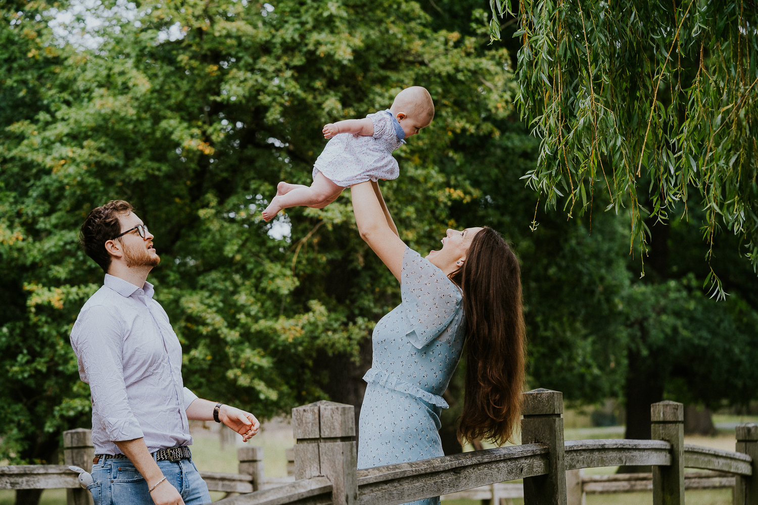 SPRING MINI PHOTO SESSIONS FAMILY ON BRIDGE IN RICHMOND PARK IN SUMMER HOLDING BABY IN AIR