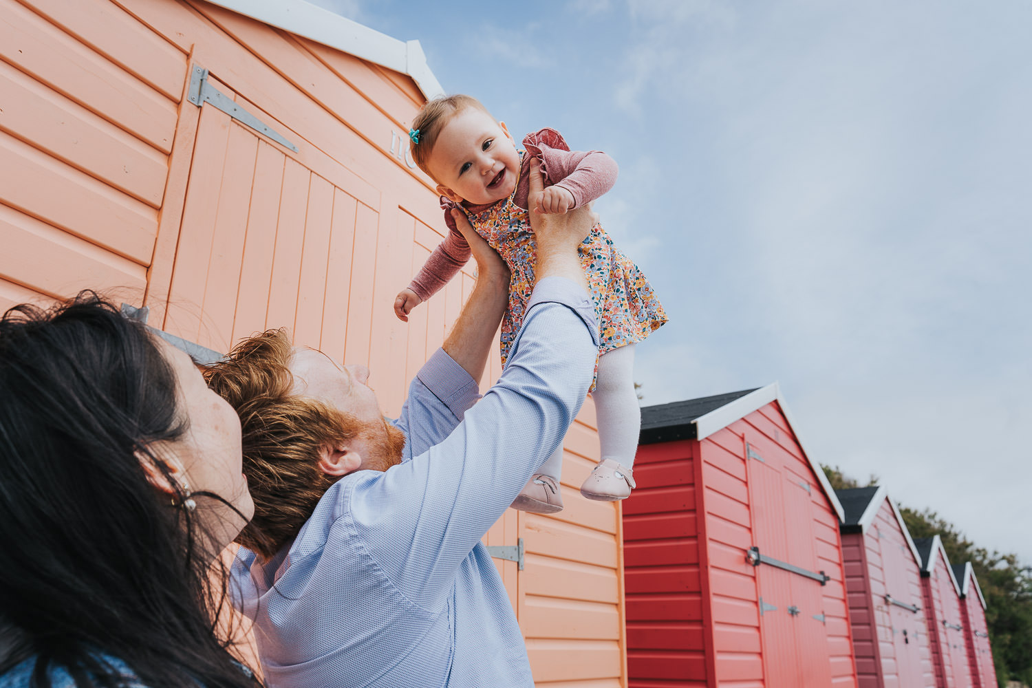 folkestone family photo shoot on the beach toddler girl with parents and beach huts in background