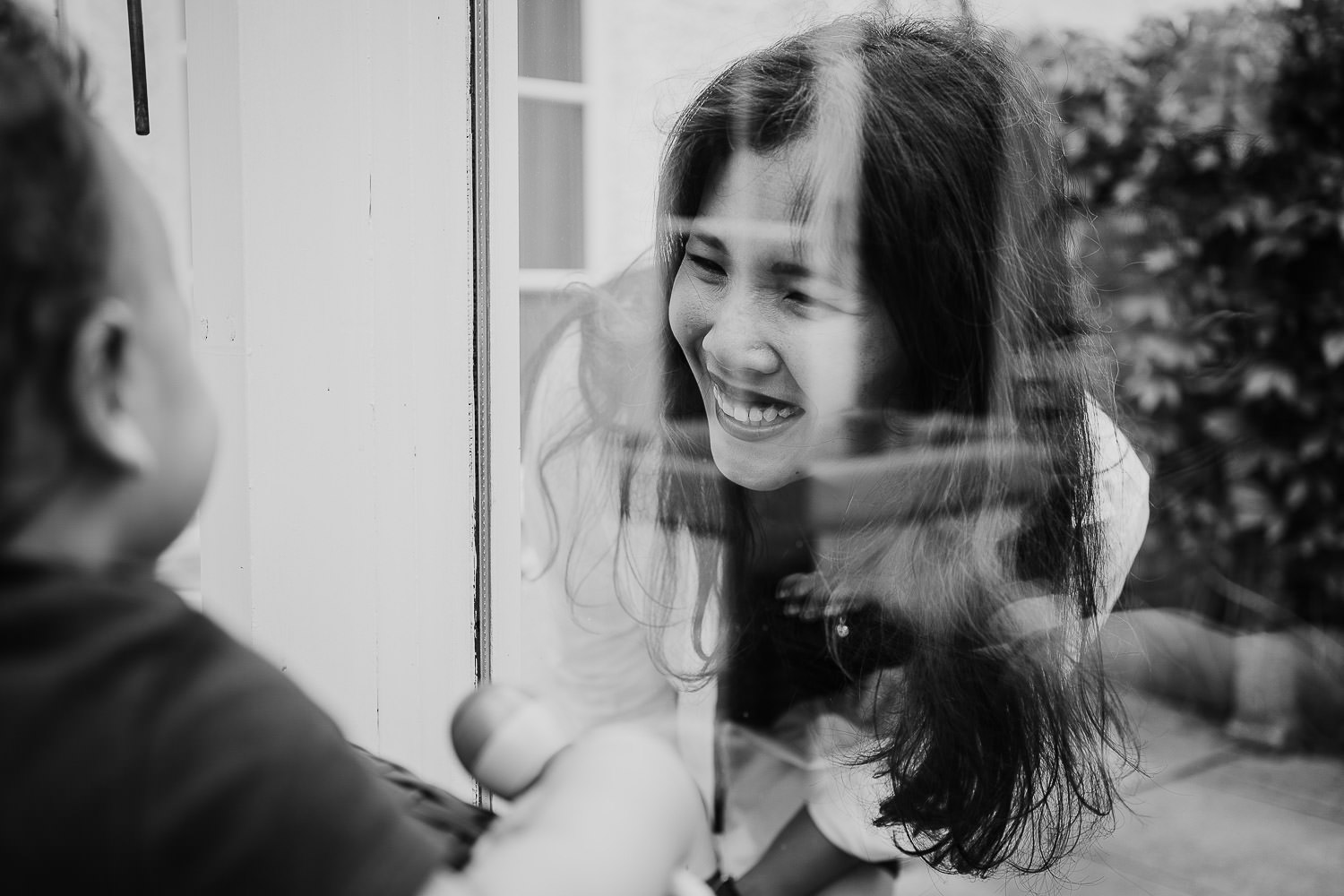 family photo shoot at home toddler boy looking at his smiling mum through a window