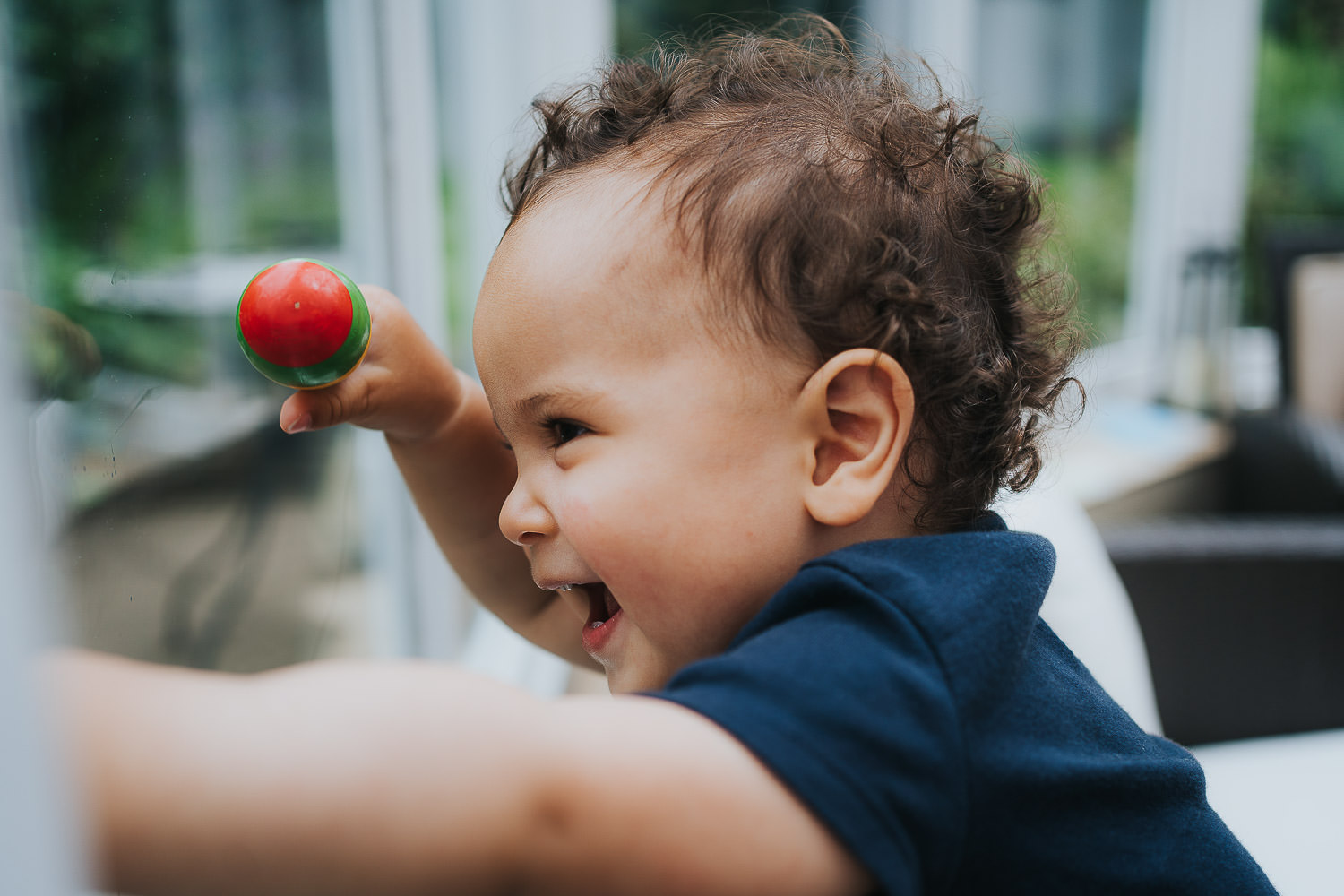 family photo shoot at home toddler boy banging on window with a rattle and laughing