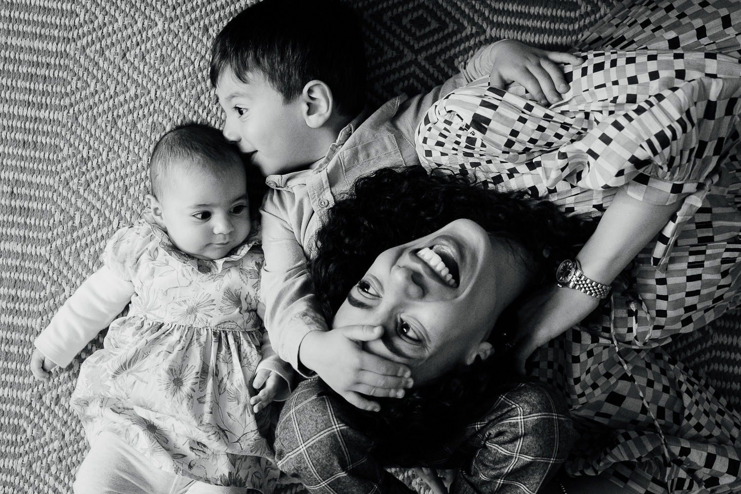 bayswater family photo shoot mother and two children lying on floor cuddling and laughing in black and white
