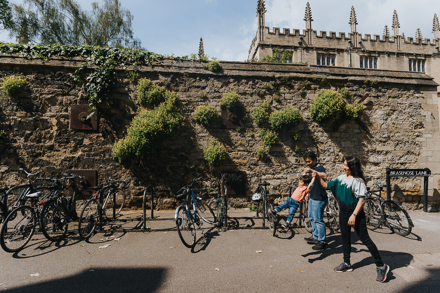 oxford family photo shoot toddler and parents walking by old wall with bikes parked next to it