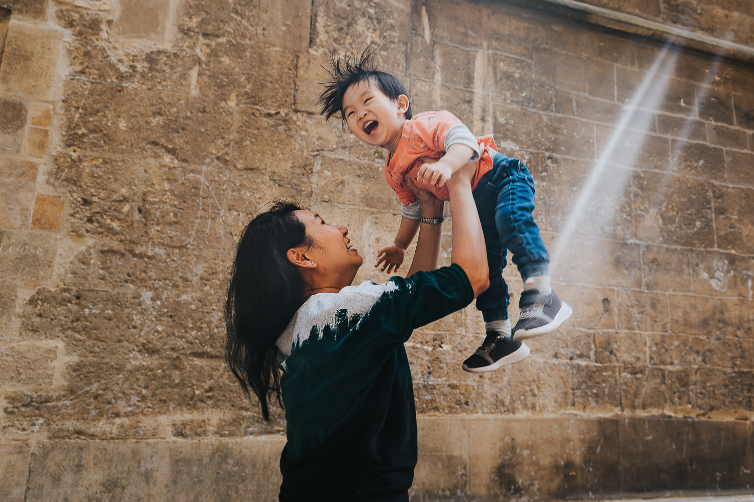 oxford family photo shoot woman throwing smiling toddler boy in the air with sun flare