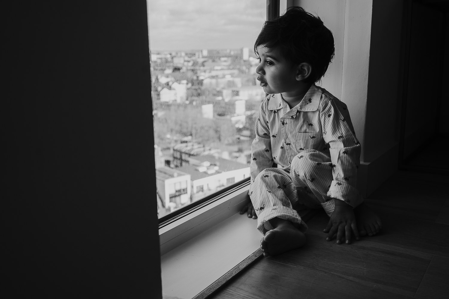 SHOREDITCH MATERNITY PHOTO SHOOT LITTLE TODDLER BOY LOOKING OUT OF LARGE APARTMENT BUILDING WINDOWS AT SKYSCRAPERS OUTSIDE
