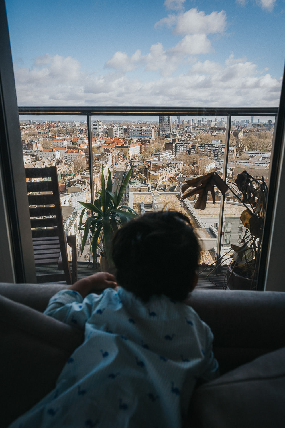 SHOREDITCH MATERNITY PHOTO SHOOT TODDLER BOY LOOKING OUT OF TALL APARTMENT WINDOW AT LONDON VIEWS OUTSIDE