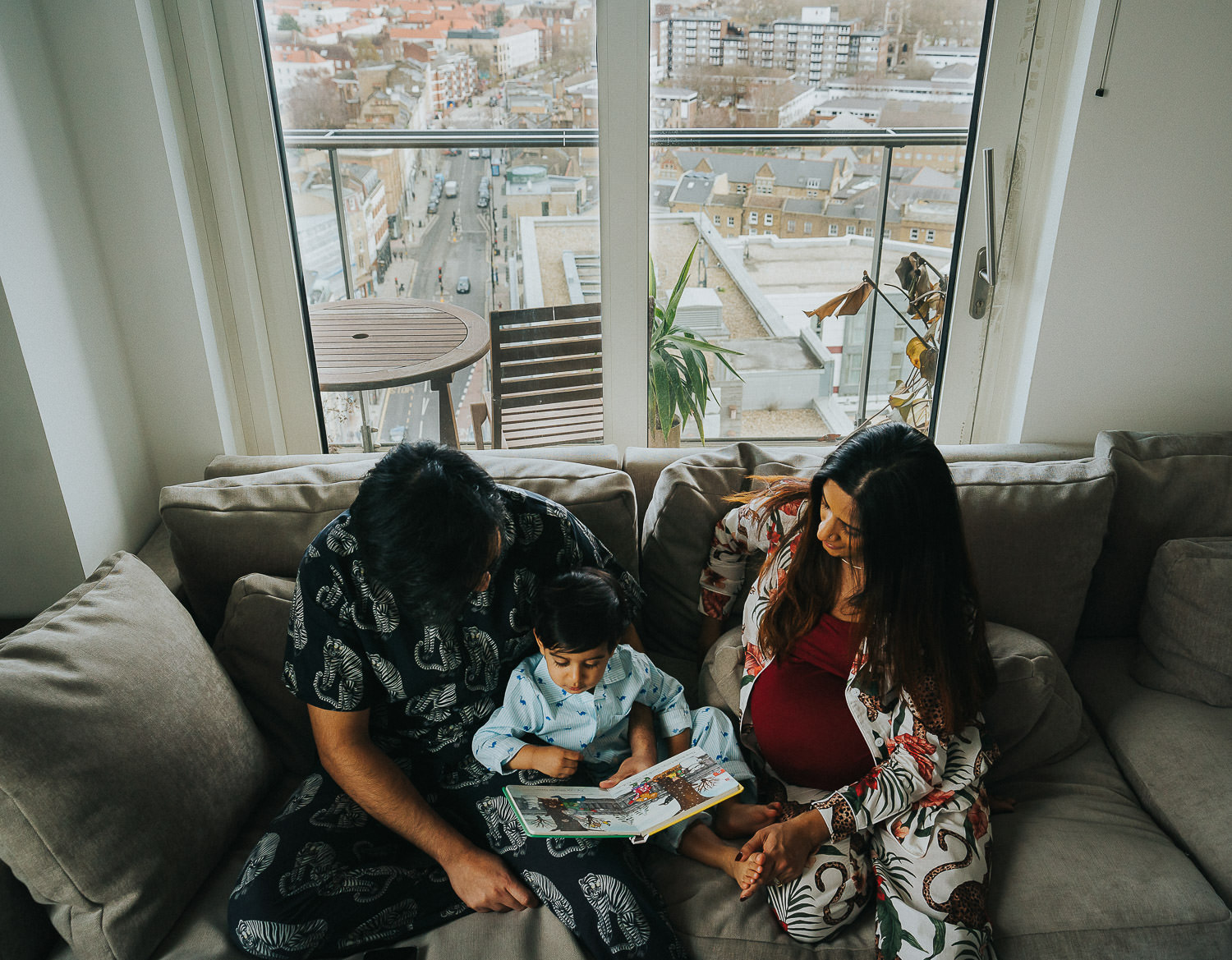 SHOREDITCH MATERNITY PHOTO SHOOT TODDLER BEING READ TO BY PARENTS ON SOFA