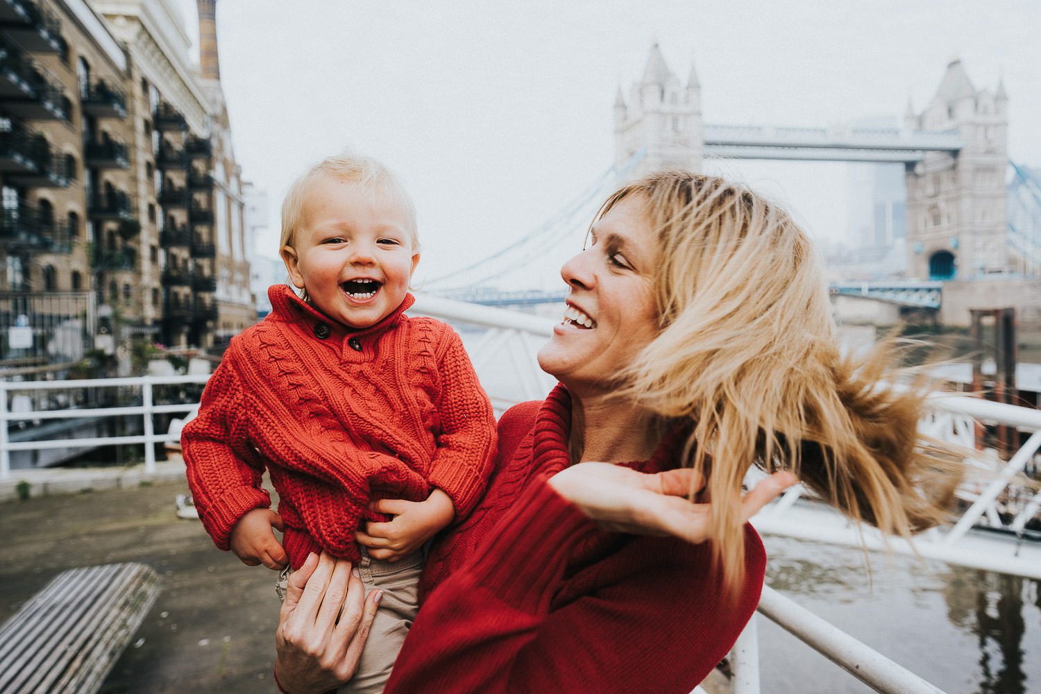 autumn mini photo shoot mother and baby son laughing in matching red sweaters by tower bridge london